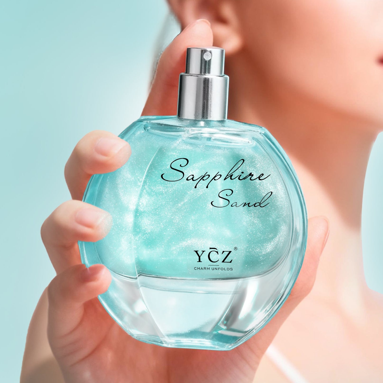 Blue perfume bottle labeled 'Sapphire Sand' by YCZ held by a person against a light blue background